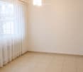 Empty room with tiled floor, white walls, large window with curtains, and a hanging light fixture.