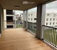 Balcony with wooden decking, metal railing, and view of surrounding buildings and greenery.