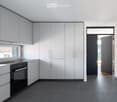 Modern kitchen with white cabinets, black oven, and dark tiled floor. Features a large window and an open doorway leading to another room.