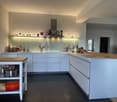 Modern kitchen with white cabinets, island, sink, and various kitchen items including pots, pans, and bottles.