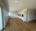Empty room with wooden floor, white walls, kitchen with white cabinets, sink, faucet, and oven, large windows, sliding door