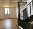 Empty hallway with wooden flooring, white walls, and a window on one side. A modern metal staircase leads upwards.