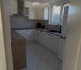 Modern kitchen with white cabinets, tiled floor, and a wooden countertop. Features include a sink with a faucet, a dishwasher, and a coffee maker on the counter.