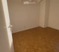 Empty room with wooden herringbone flooring, white walls, and exposed wooden beams on the ceiling. No furniture or equipment present.