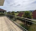 Balcony with tiled floor and metal railing, overlooking a residential area with houses, palm trees, and a field.