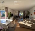 Modern living room with a large window offering a scenic view, featuring a cream-colored sofa, a glass dining table with white chairs, a fireplace, and decorative plants.