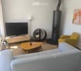 Modern living room with a grey sofa, wooden coffee table, armchair, TV, floor lamp, and a sleek black fireplace.