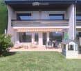 Well-maintained garden with a lawn, patio area with chairs and a table, and a small playhouse.