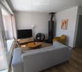 Modern living room with light grey sofa, wooden coffee table, TV stand, armchair, floor lamp, and a modern fireplace.