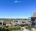 Balcony overlooking a residential neighborhood with houses, trees, and distant cityscape under a clear blue sky.