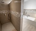 Modern bathroom with a bathtub and separate shower area, featuring beige tiles and geometric patterned borders.