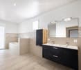 Modern bathroom with a bathtub, double sink, large mirror, and dark wooden cabinet.