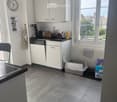 Modern kitchen with white cabinets, black countertop, sink, dishwasher, and various appliances. Features a tiled floor, a window with a view, and a cat litter box in the corner.