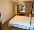 Spacious bedroom with wooden flooring, large bed with white bedding, nightstand, and open door leading to another room.