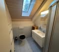 Cozy attic bathroom with skylight windows, white tiled walls, a toilet, a sink with a mirror, and a small wooden cabinet.