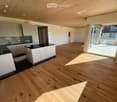 Empty room, hardwood floors, white cabinets, modern kitchen with black countertops, sliding glass door to balcony