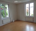 Empty room with wooden flooring, white walls, and large windows with radiators beneath them.