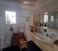 Bathroom with a double sink, mirror cabinet, towel on a rack, small wooden stool, and a shower area with a window.
