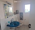 Cozy bathroom with a blue sink, white toilet, decorative mirror, and a small window letting in natural light.