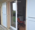 Balcony with glass sliding doors leading to a small indoor space, featuring a wooden floor, a red folding chair, and a small table with a lamp.