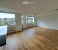 Empty room with wooden flooring, large windows offering a scenic view, and white walls.