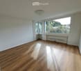 Empty room with wooden flooring, white walls, large windows, and radiators. No furniture or equipment present.