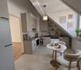Modern kitchen with white cabinets, stainless steel appliances, a small dining area with a round table and chairs, and decorative items on the windowsill.