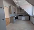Empty kitchen with white cabinets, a countertop, and a sink. The space features wooden flooring and large windows allowing natural light to enter.