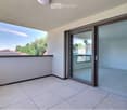 Balcony with tiled floor, large glass sliding doors, and a view of the surrounding area with trees and rooftops.