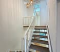 Modern staircase with wooden steps, white railing, and pendant lights, leading to a bright, open area with skylights.