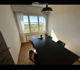 Bright dining area with a black dining table, chairs, a cup, and a radiator near a large window offering a scenic view.