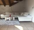 Modern living room with a white sectional sofa, wooden coffee table, floor lamp, and a shaggy rug on tiled flooring.