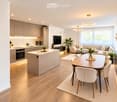 Modern open-plan living and dining area with a kitchen island, sofa, dining table, and various decorative elements including potted plants and a television.