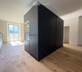 Modern kitchen with dark grey cabinets, light wooden flooring, and a large window offering a scenic view.