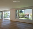 Empty room with wooden flooring, large windows, and sliding doors leading to an outdoor area.