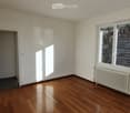 Empty room with wooden flooring, white walls, and large windows allowing natural light. Features a radiator and an open doorway leading to another space.