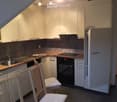 Modern kitchen with white cabinets, wooden countertops, stainless steel sink, oven, and two wooden chairs.