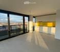 Modern, unfurnished kitchen with white cabinets, a yellow backsplash, and a large window offering a city view. The space includes a sink and faucet, with a balcony accessible through large glass doors.