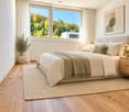 Modern bedroom with a large bed, nightstands, lamps, a rug, and a potted plant near the window offering a scenic view.