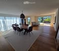 Bright dining area with wooden flooring, large windows, and a view of the outdoor patio. Features a dining table with chairs, a sofa, and a refrigerator.