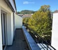 Balcony with tiled floor, metal railing, and scenic view of trees and buildings.