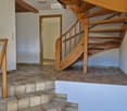 Hallway with a wooden staircase leading upwards, tiled floor, and white walls.