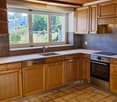 Modern kitchen with wooden cabinets, white countertops, stainless steel appliances, and a large window overlooking a garden.