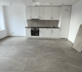Empty kitchen with white cabinets, stainless steel appliances, and a large concrete floor. No furniture or items present.