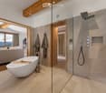 Modern bathroom with a freestanding bathtub, glass-enclosed shower, wooden accents, and a view of a mountain landscape through large windows.