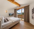 Cozy bedroom with a large bed, pillows, wall-mounted TV, and a scenic mountain view through large windows with curtains.