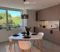 Modern kitchen and dining area with a white dining table, four white chairs, grey cabinets, a sink, and a pendant light fixture.
