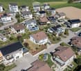 Aerial view of a residential neighborhood with multiple houses, solar panels on roofs, driveways, and surrounding greenery.