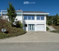 Modern two-story house with white exterior, large windows, garage, and raised ground floor entrance.
