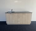 Modern kitchen island with light wood cabinets, stainless steel sink, and faucet.